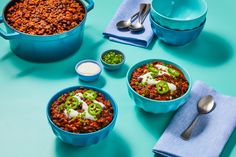 two blue bowls filled with chili, beans and sour cream on top of a turquoise table