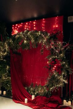 a red curtain with christmas lights hanging from it's side and candles on the floor