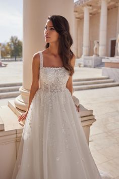 a woman in a white wedding dress standing next to a pillar and looking off into the distance