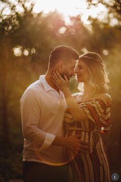 a man and woman standing next to each other in front of trees with the sun behind them