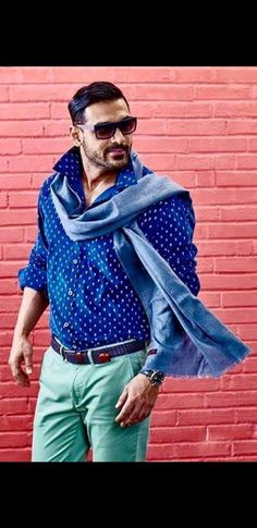 a man standing in front of a red brick wall wearing sunglasses and a blue scarf