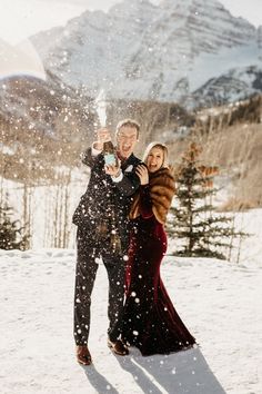 a man and woman are standing in the snow with their arms around each other, making a toast