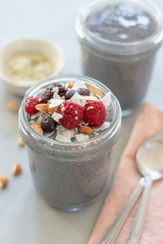 two jars filled with granola and fruit on top of a table next to spoons