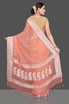 Look attractive on festive occasions in this peach georgette chiffon saree with silver zari border and buta. It comes with a matching blouse piece. Shop handwoven sarees in USA from Pure Elegance. Disclaimer: The actual product may vary slightly from the image. These are custom orders, hence expect slight variation in color, placement of the motif or buta. ESTIMATED DELIVERYBecause this is a custom order, it would take about 4 weeks from the date of purchase. RETURN POLICYThis product is a custo Indian Designer Sarees, Shades Of Peach, Fashion Journals, Traditional Fabric, Chiffon Saree, Banarasi Sarees, Georgette Sarees, Indian Design, Sarees Online