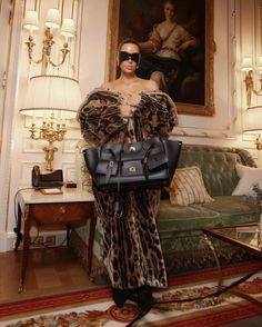 a woman standing in front of a painting holding a black purse and wearing leopard print dress