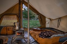 an open tent with a stove and sleeping bag in the foreground, next to it