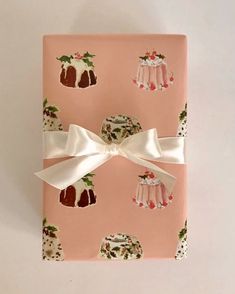 a pink wrapping paper with christmas puddings and holly on it, tied to a white ribbon