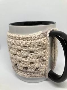 a crocheted coffee cup holder with a black handle and white mug in the middle