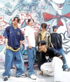 a group of young men standing next to each other in front of a graffiti covered wall