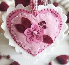 a pink heart shaped ornament hanging from a red and white ribbon on a table