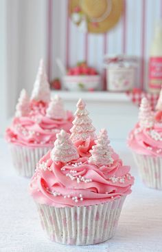 three cupcakes with pink frosting and white trees on top are sitting on a table