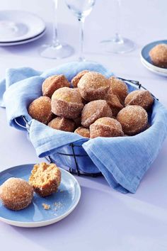 a basket filled with sugar covered donuts on top of a blue plate next to plates