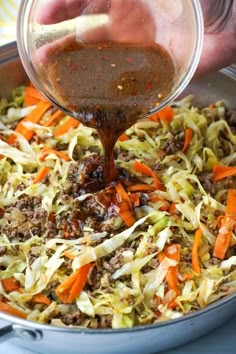 someone pouring dressing into a pot filled with cabbage, carrots, and shredded meat