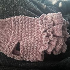 a pink knitted object laying on top of a black blanket with ruffles