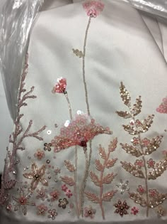 an embroidered white cloth with pink flowers and sequins on the side, sitting in a plastic bag