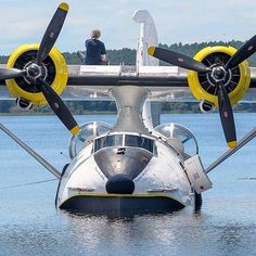 a propeller plane sitting on top of a body of water next to a man standing on the back of it