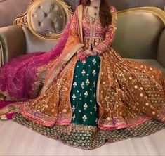 a woman sitting on top of a couch wearing a green and gold dress with pink dupatta