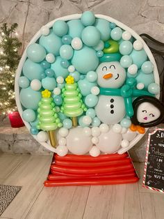 a snowman and penguin balloon display in front of a christmas tree with a chalkboard sign