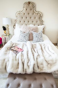 a bed with white fur and pillows on top of it next to a nightstand table