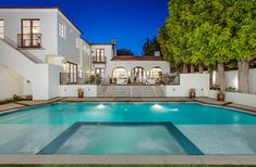 an outdoor swimming pool in front of a large white house at night with lights on