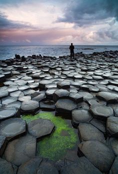 a man standing on top of a rock covered beach next to the ocean under a cloudy sky