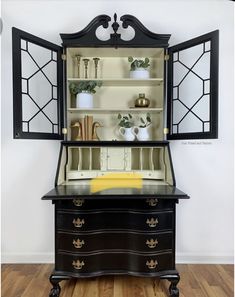 an old fashioned dresser with glass doors and gold trimmings on the top, in front of a white wall