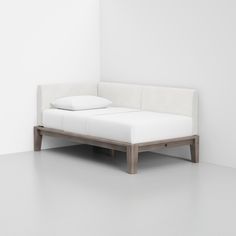 a white bed sitting in the middle of a room next to a wall with two pillows on top of it