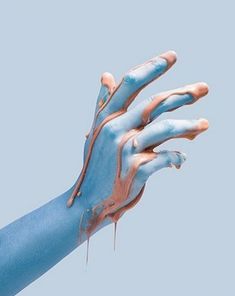 a person's hand with blue and orange paint on it, holding something in the air