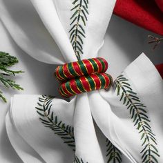 two napkins are wrapped in red and green fabric with pine branches on them, along with evergreen needles