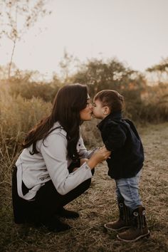 a mother kissing her son in the face while sitting on the ground with tall grass