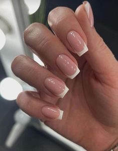 a woman's hand with french manies and white tips on her nails, in front of a mirror