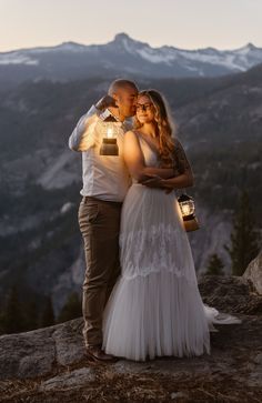 a man and woman standing next to each other on top of a mountain holding lanterns