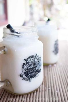 two glass jars sitting on top of a table next to each other, one filled with milk and the other empty