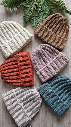 four knitted hats sitting on top of a wooden table next to a fern plant