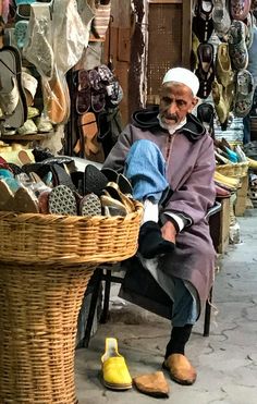 an old man sitting in front of a basket full of shoes