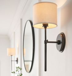 a wall mounted light next to a mirror and potted plant in a white room