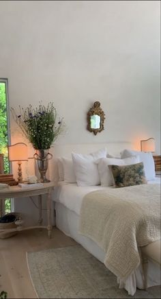 a white bed sitting in a bedroom next to a table with flowers on top of it