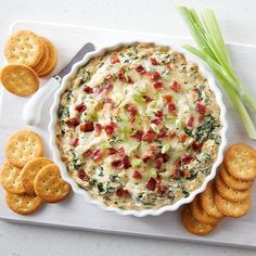 a bowl of dip with crackers and celery next to it on a cutting board