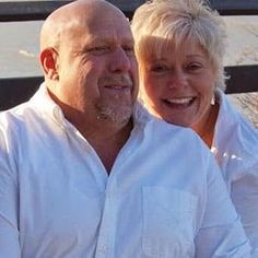 a man and woman sitting next to each other on a bench by the water smiling