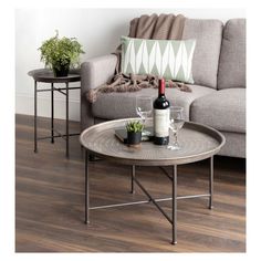 a table with two wine glasses and a bottle on it next to a gray couch