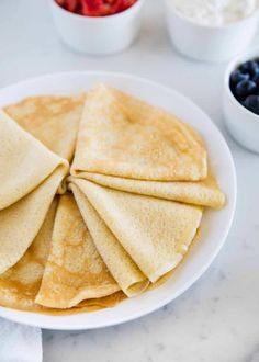 pancakes on a white plate with blueberries and syrup in a bowl next to it