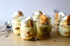 four desserts in small glass jars on a wooden table with spoons and utensils