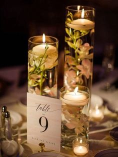 two tall vases filled with flowers and candles on top of a white table cloth