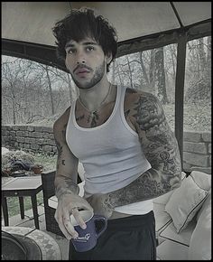 a man with tattoos on his arm holding a cup and an object in his hand