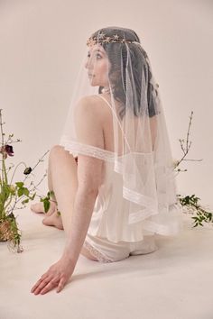 a woman sitting on the ground wearing a veil and holding flowers in her hand with both hands