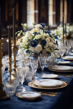 a table set with blue and white flowers, gold place settings and silver candlesticks