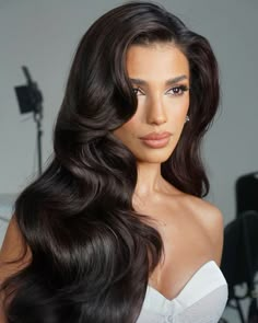 a woman with long dark hair wearing a white dress and posing in front of a camera