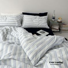 an unmade bed with blue and white striped comforter, pillows, and books