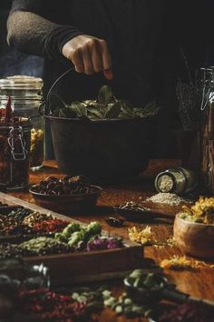 a person preparing food in a bowl on top of a wooden table with spices and seasonings