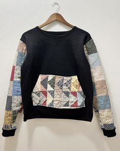 a black sweatshirt with multicolored patchwork on the front and back, hanging up against a white wall